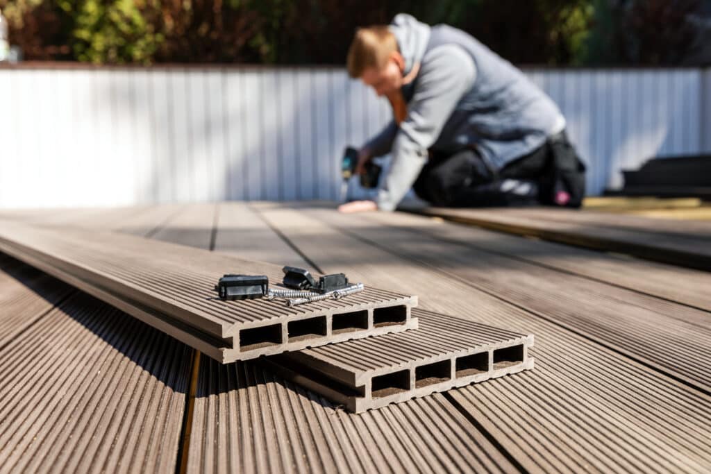 Installation de terrasse : un homme pose des lames en bois composite. Vis et clips en gros plan sur les planches.