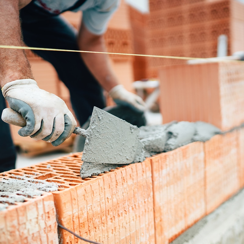 Un maçon ganté applique du mortier sur des briques rouges avec une truelle pour construire un mur. Travaux de construction.